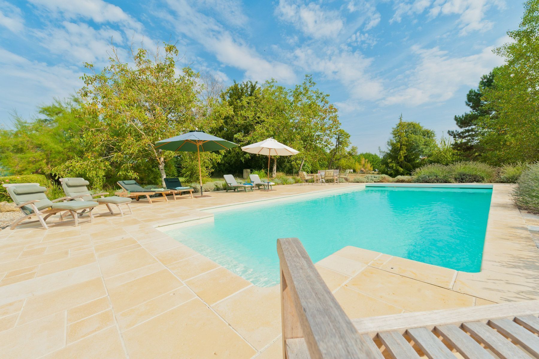 A swimming pool with lounge chairs and umbrellas, surrounded by trees.