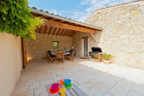 A stone building with a wooden pergola, outdoor seating, and a barbecue area.