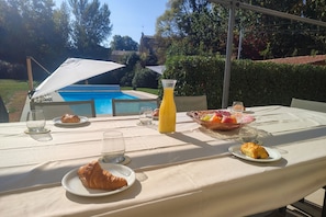 Ein Tisch draußen mit Pool im Hintergrund, eine Orangensaftflasche und Tellern mit Essen.