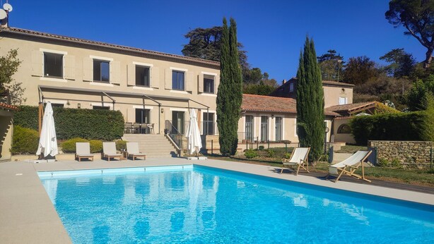 Ein Pool mit Liegestühlen, ein Gebäude mit einem Ziegeldach und eine Steinsäule.