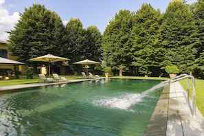 A swimming pool with lounge chairs and umbrellas, surrounded by trees.