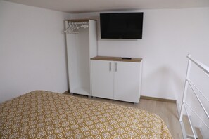 Een slaapkamer met een bed, een kledingkast, een televisie en een witte metalen ladder.