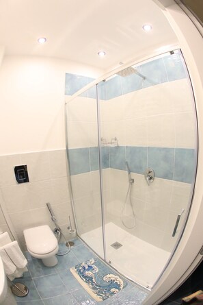 Un bagno con doccia vetrata, un water e un tappetino blu con motivo decorativo.