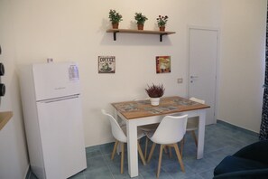Una cocina compacta con un refrigerador blanco, una mesa de madera con sillas y una estantería con plantas en macetas.