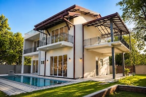 Une maison à deux étages dotée d’un balcon, d’une piscine et d’un jardin bien entretenu.