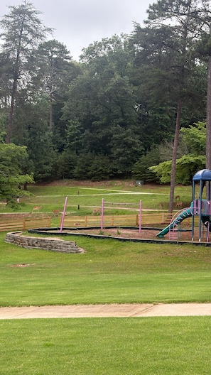 Un parque con un área de juegos, una zona cercada y un campo cubierto de césped.