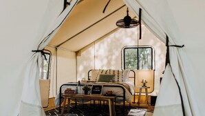 Una habitación con carpa, una cama, una mesita con un cartel, una lámpara y una ventana.