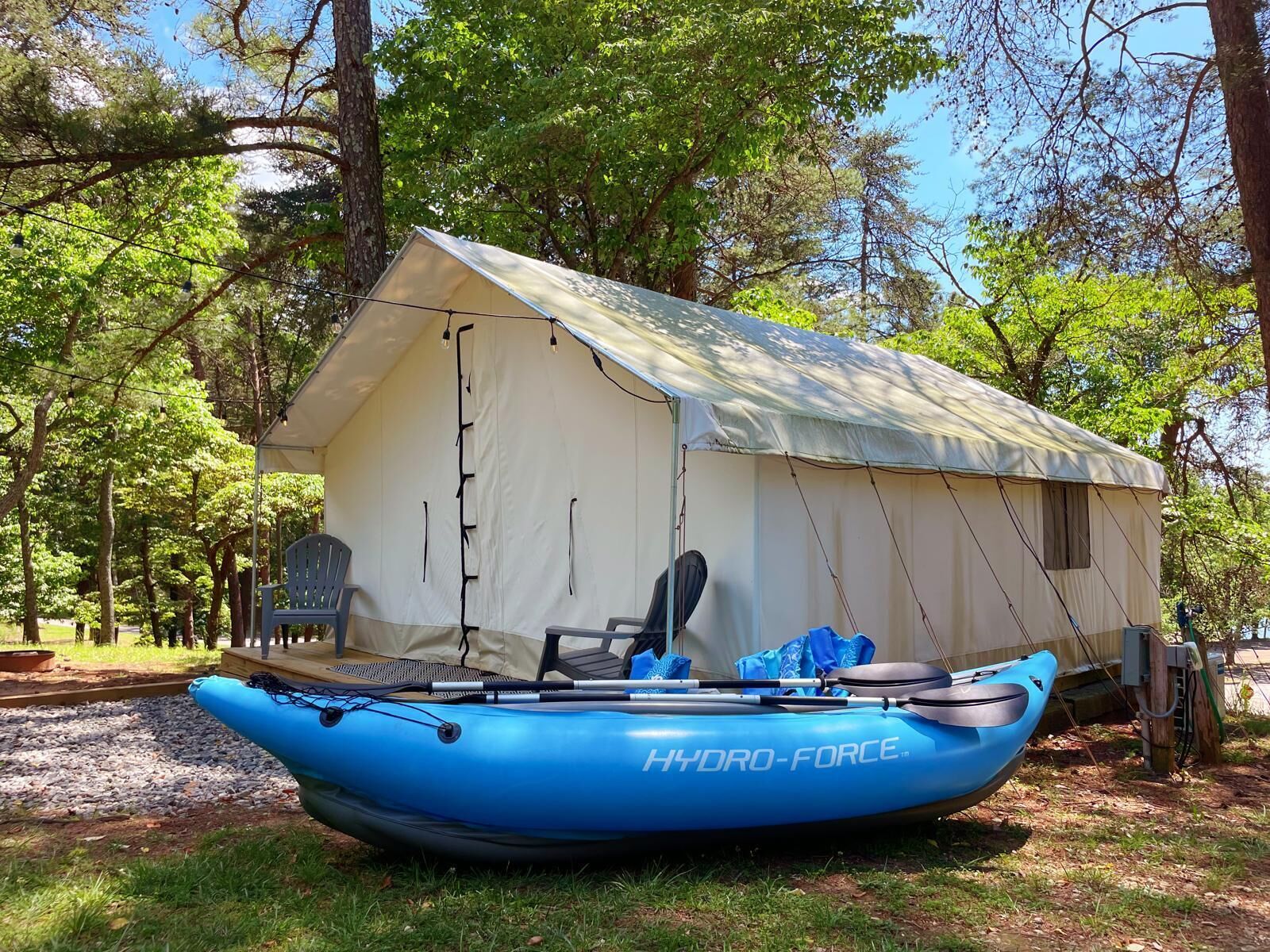 Uma tenda com um caiaque azul por dentro, rodeada por árvores.
