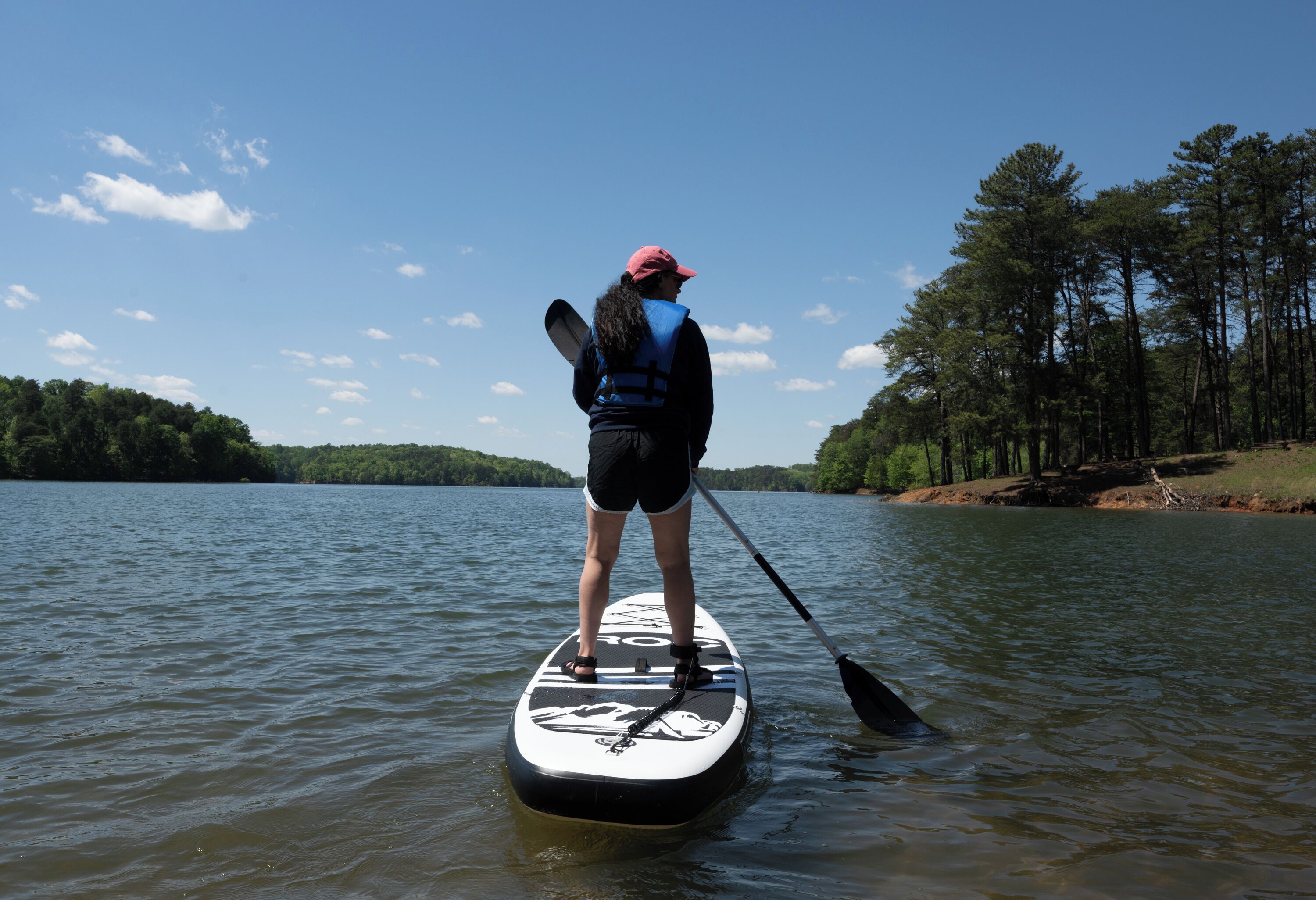 A person standing on a paddleboard in a body of water with trees in the background.