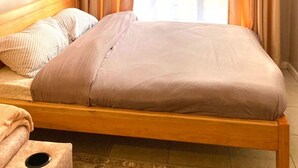 Ein Einzelbett mit Holzrahmen, Kopfteil und einer beigefarbenen Bettdecke.