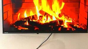 Ein Flachbildfernseher an der Wand, der einen Kamin mit sichtbaren Flammen zeigt.