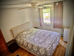 Ein Schlafzimmer mit einem Bett, einem Deckenventilator, einem Fenster mit Vorhängen und einer Heizung.