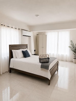 Un dormitorio con cama, mesita de noche, armario y una planta en maceta.