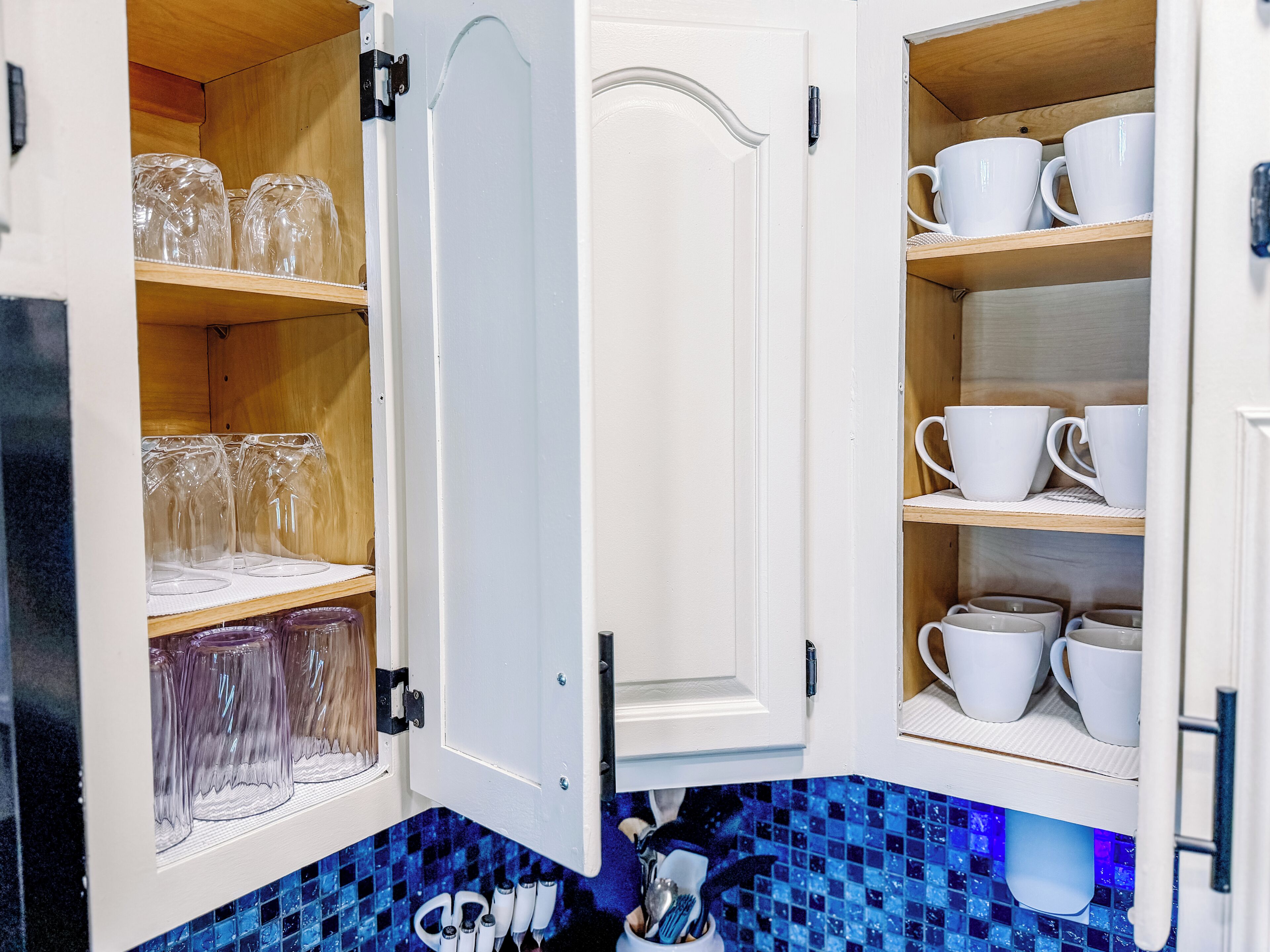 Una cocina con armarios abiertos que contienen cristalería transparente y tazas blancas.