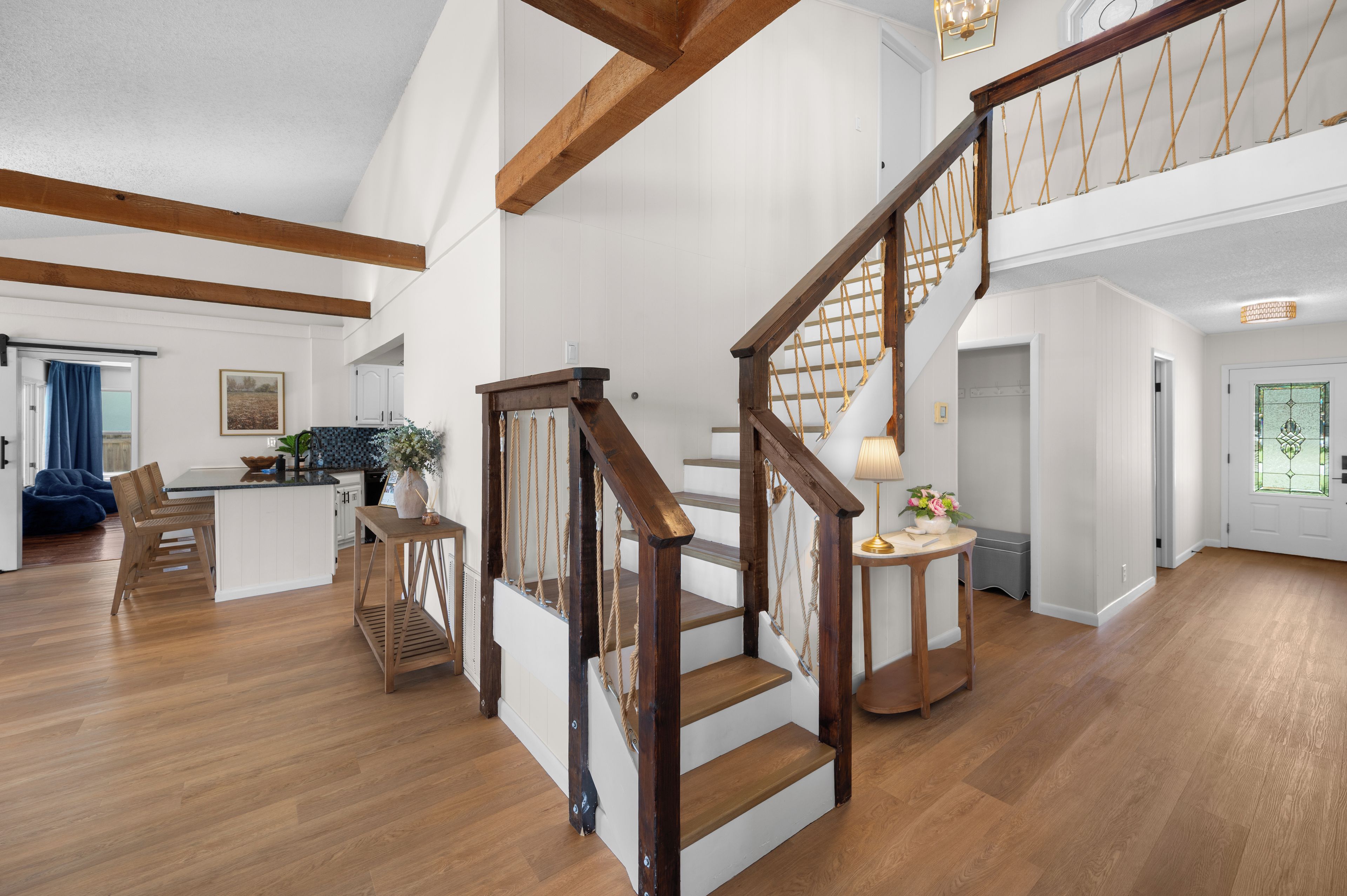 Amplia sala de estar con escalera de madera, cocina con muebles blancos y comedor con una silla azul.
