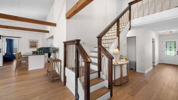 Amplia sala de estar con escalera de madera, cocina con muebles blancos y comedor con una silla azul.