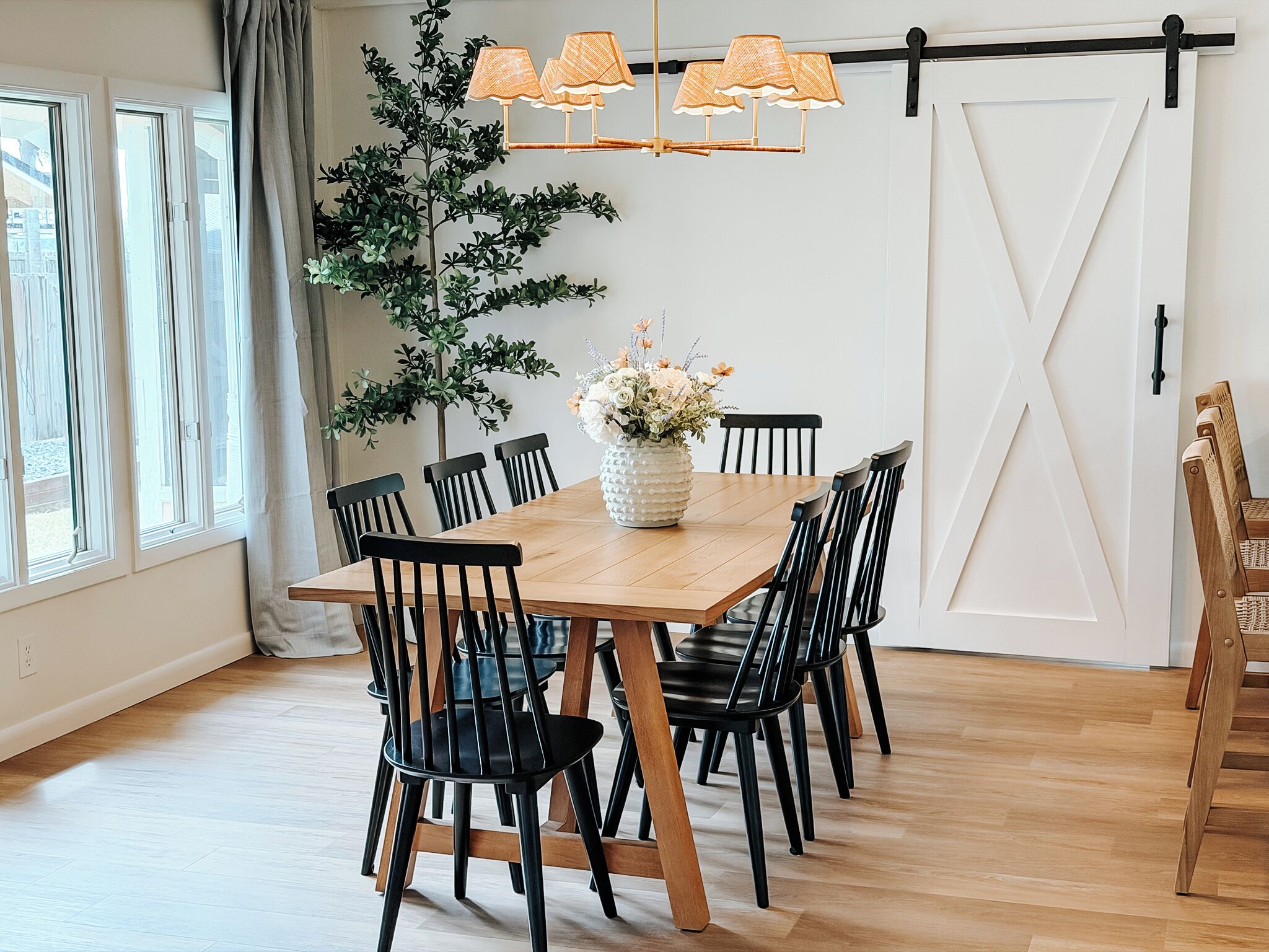 A dining area with a wooden table, black chairs, a potted plant, and a sliding barn door.