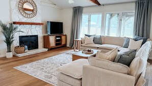 A living room with a fireplace, sofa, TV, and large windows.
