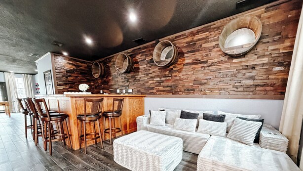 A modern kitchen with a bar area, wooden bar stools, and a seating area with cushions.