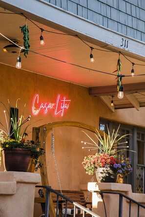 Ein Gebäude mit einer Neonreklame mit dem Schriftzug 'Casa Lita', Lichterketten im Freien und Topfpflanzen.