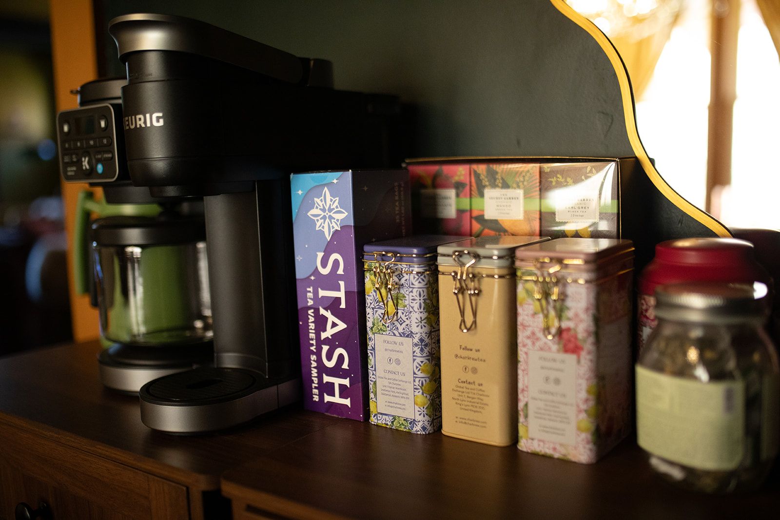A coffee maker, a box labeled 'STASH,' and several tins on a wooden surface.