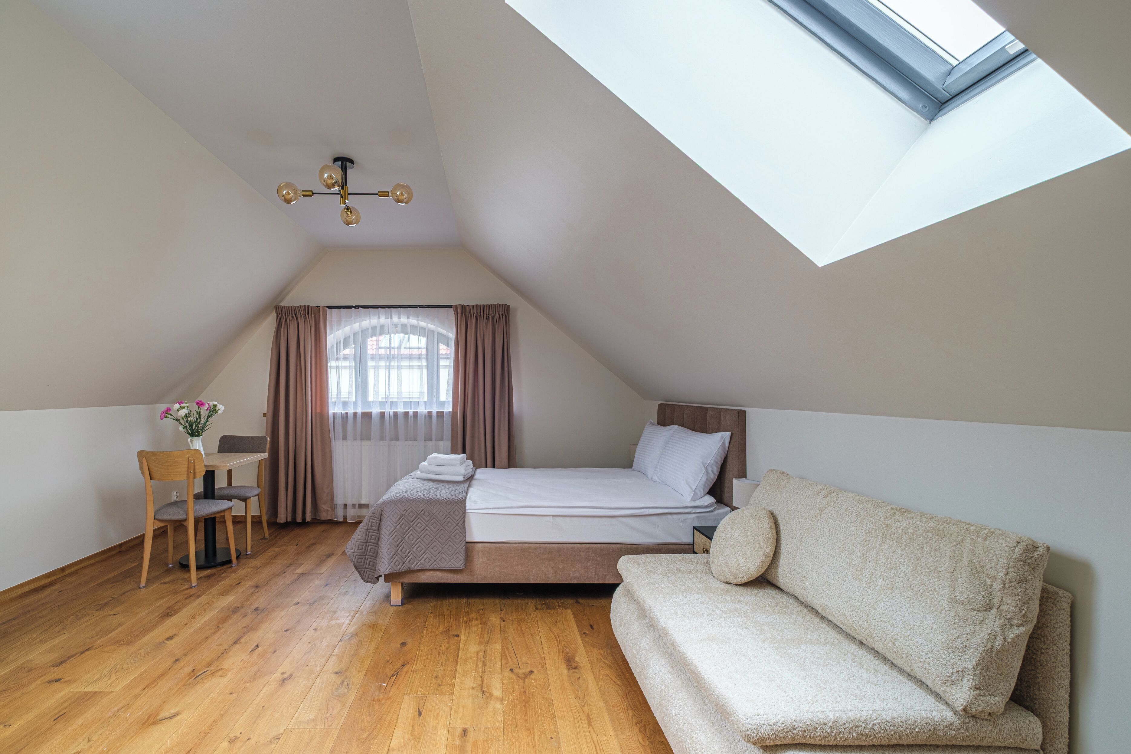 A bedroom with a skylight, a bed, a sofa, a desk, and a chair.