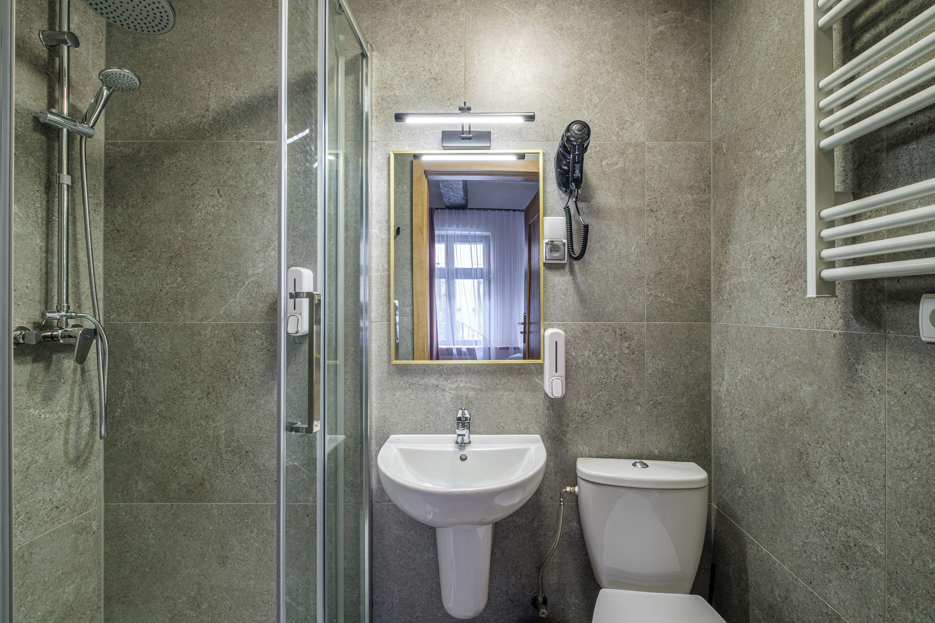 Casa de banho com cabine de chuveiro em vidro, lavatório suspenso, sanita e secador de cabelo, além de porta-toalhas.