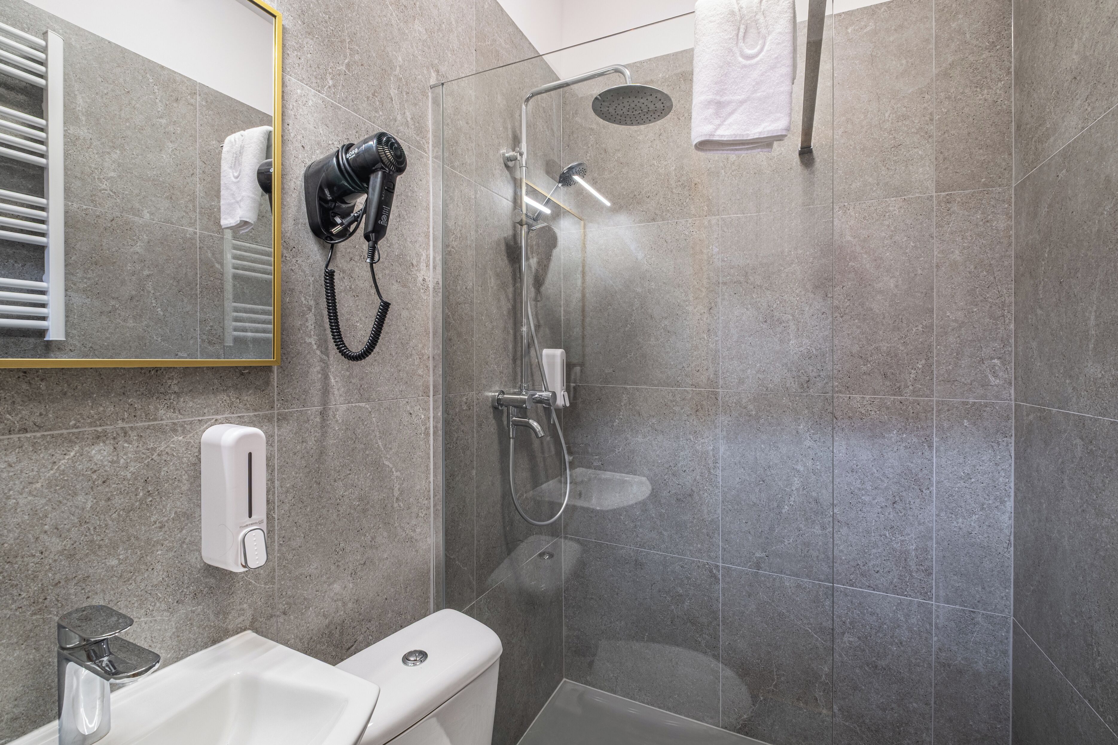 Un bagno moderno con doccia vetrata, asciugacapelli, porta asciugamani e dispenser per sapone.