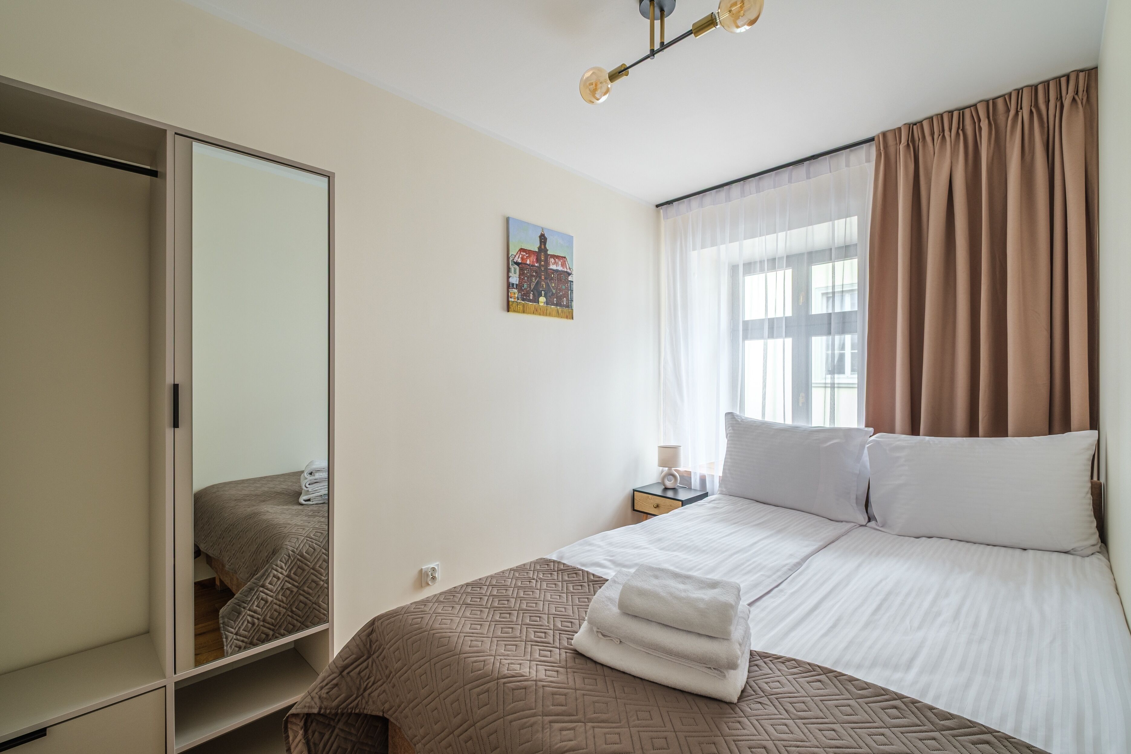 Une chambre d’hôtel avec un lit, une table de chevet, une commode, un miroir, une fenêtre avec des rideaux et un tableau au mur.