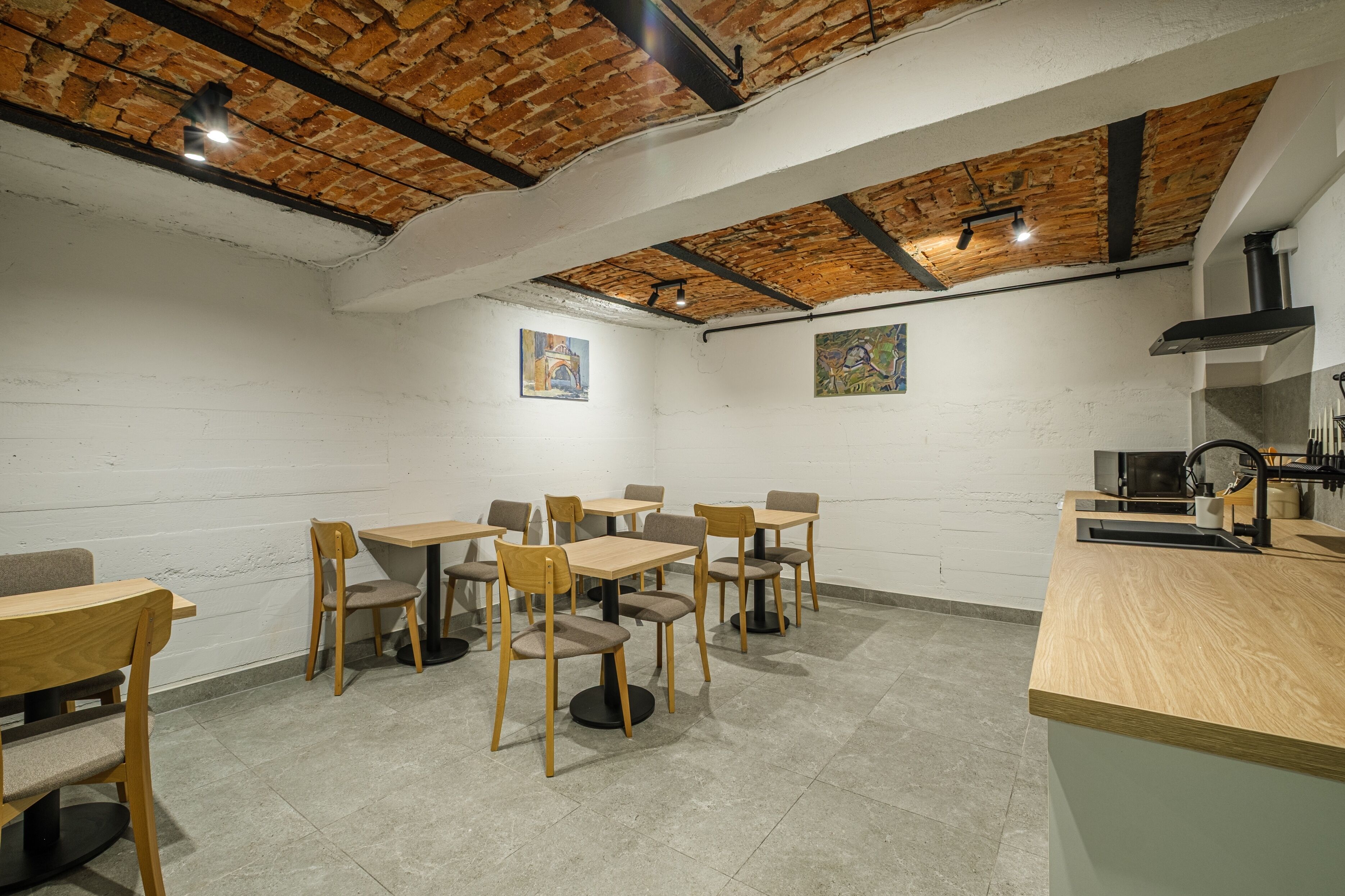 Un comedor con mesas y sillas de madera, techo de ladrillo y pared blanca con obras de arte.