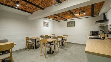 Un comedor con mesas y sillas de madera, techo de ladrillo y pared blanca con obras de arte.