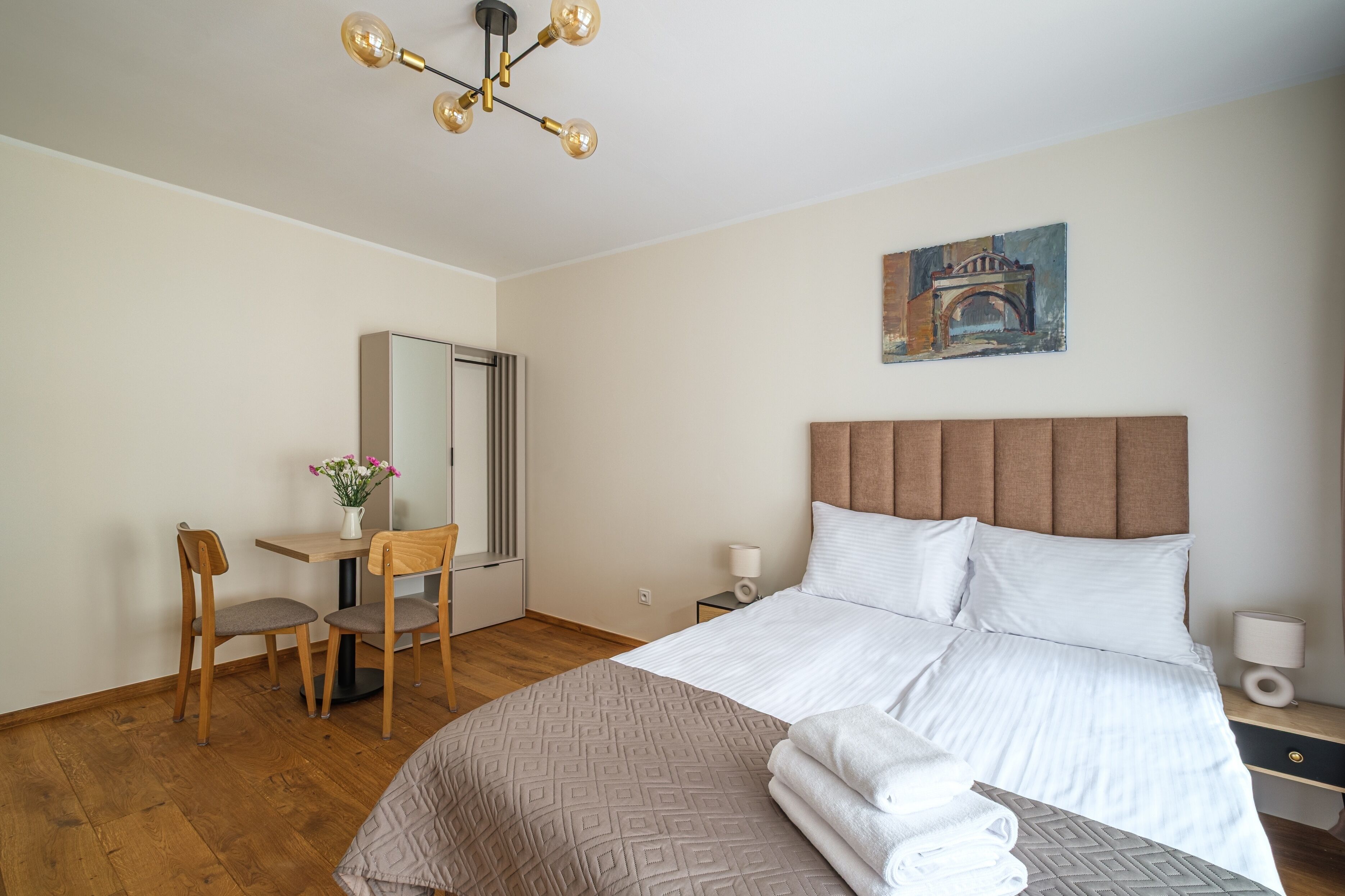 Habitación de hotel con cama, escritorio, silla, un cuadro y una lámpara de araña moderna.