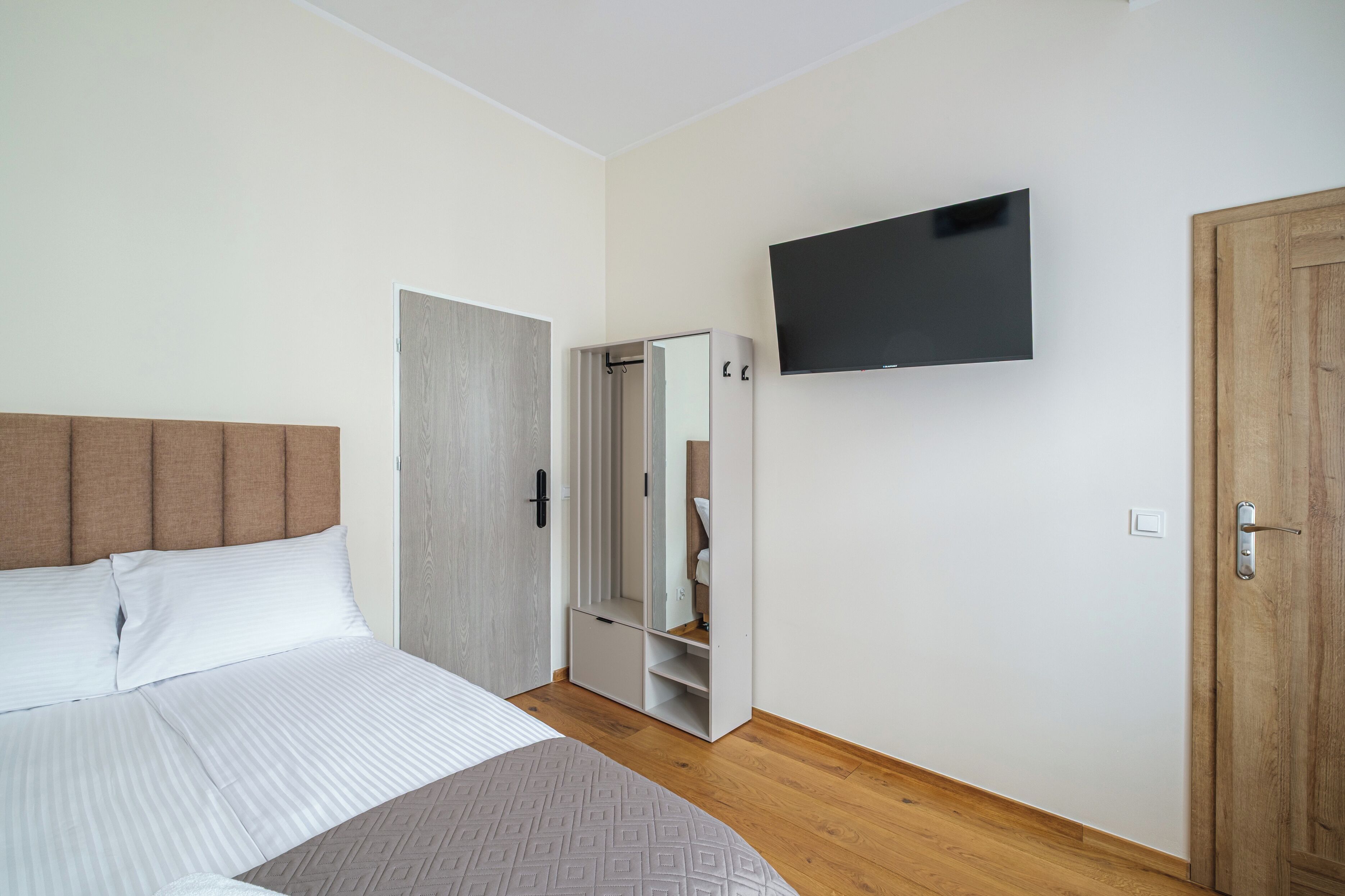 A bedroom with a bed, a wardrobe, a mirror, and a television.
