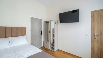 A bedroom with a bed, a wardrobe, a mirror, and a television.