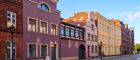 A street with buildings, including a pink building with a sign that reads 'Apartmenty Gdansk Gród'.