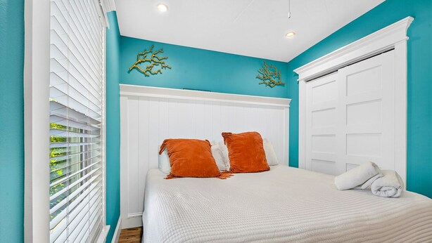 Un dormitorio con una cama, dos almohadas naranjas, un cabecero blanco y una puerta blanca.