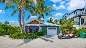 Una propiedad residencial con garaje, un carrito de golf y un jardín bien cuidado con palmeras y plantas tropicales.