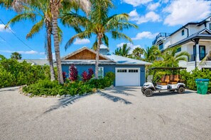 Ein Wohnhaus mit Garage, Golfmobil und einem gepflegten Garten mit Palmen und tropischen Pflanzen.