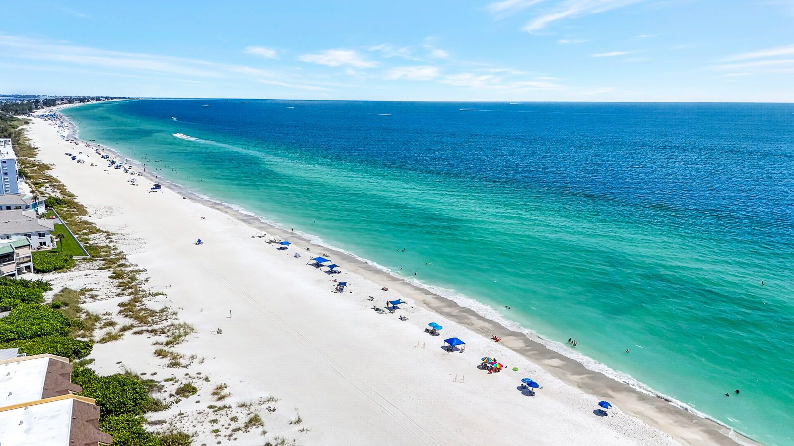 A beach with a long stretch of sand, a few umbrellas, and a few people.