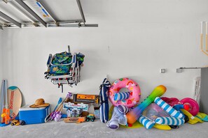Eine Garage mit Deckenventilator, einem blauen Kühlkoffer, einem Fahrrad, einem Helm, einem Surfbrett und diversen Sportgeräten.
