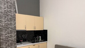 Una cucina moderna con mobili color beige, un piano di lavoro nero e un backsplash in marmo. Si vede un divano grigio e un piccolo tavolo rotondo con top in marmo.