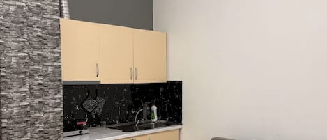 Una cocina moderna con armarios color beige, encimera negra y salpicadero de mármol. Hay un sofá gris y una pequeña mesa redonda con tapa de mármol.