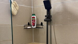 Una zona doccia con soffione a mano, una bottiglia di sapone Palmolive e un portasciugamani.