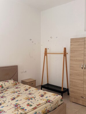 Quarto com cama, guarda-roupa de madeira, mesa de cabeceira e parede decorada com adesivos de estrelas e nuvens.