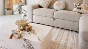 Een woonkamer met een bank, een grote spiegel, een schilderij en een bijzettafeltje met decoratieve objecten.