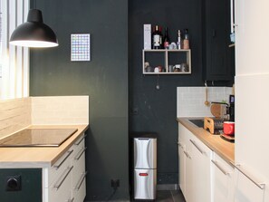Une cuisine compacte dotée d’un réfrigérateur en acier inoxydable, de plans de travail en bois et d’un luminaire suspendu.