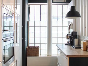 Eine Küche mit Backofen, Kaffeemaschine und einem großen Fenster mit Jalousien.