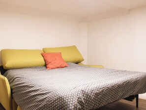 Ein Bett mit einem gemusterten Überwurf, zwei Kissen und ein gelber Sessel.