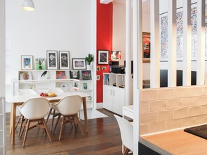 Eine moderne Küche mit weißen Schränken, einer roten Akzentwand und einem Essbereich mit weißem Tisch und Stühlen.