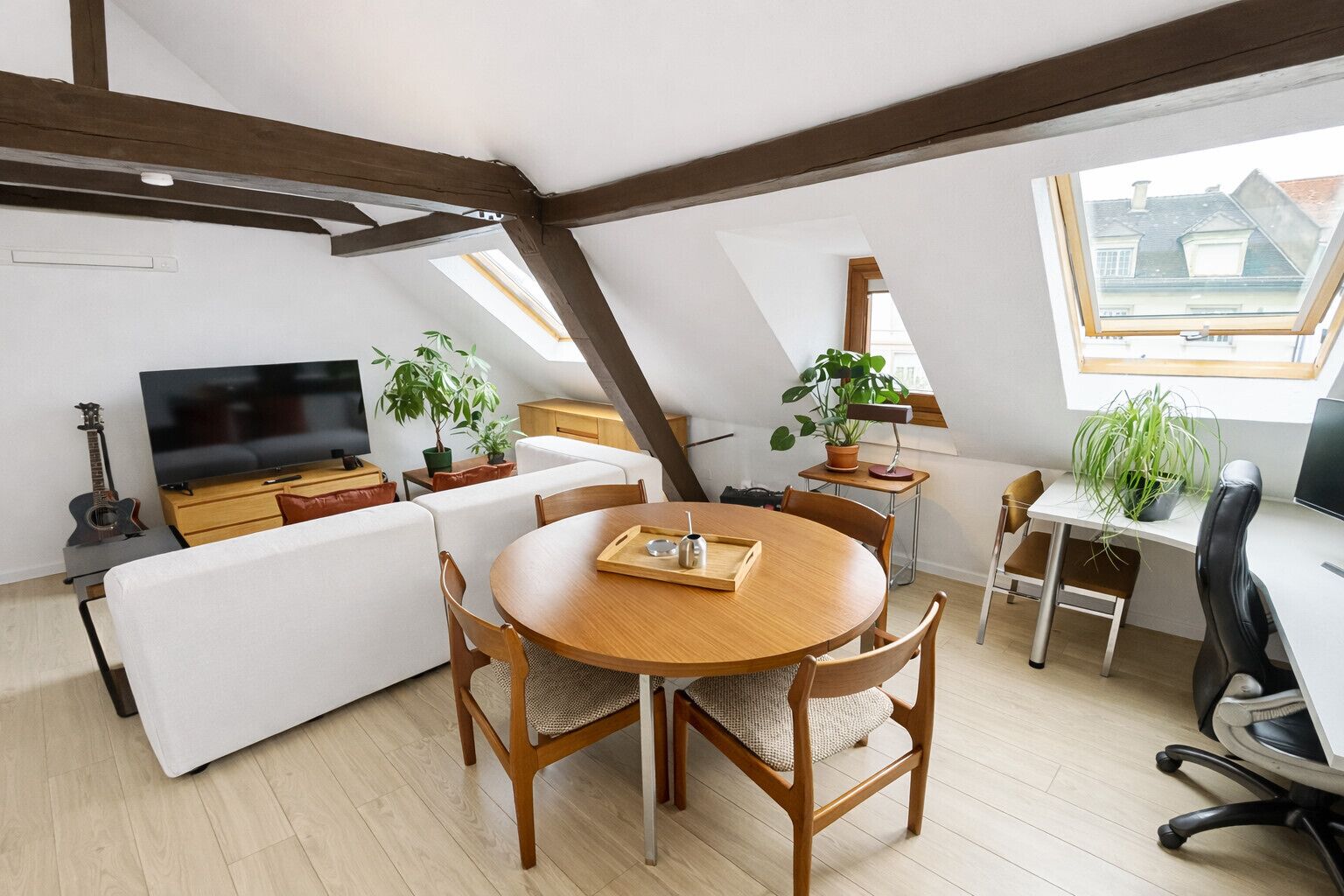 A loft-style room with a dining table, chairs, a sofa, a TV, and potted plants.